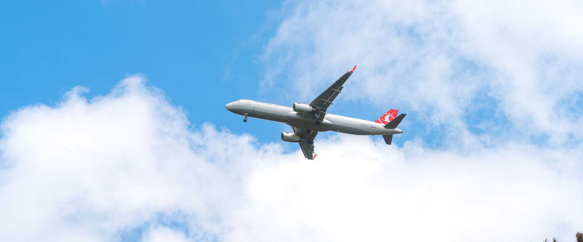 Ein Verkehrsflugzeug gleitet durch einen klaren blauen Himmel mit vereinzelten Wolken und fängt so die Essenz des Fliegens ein.