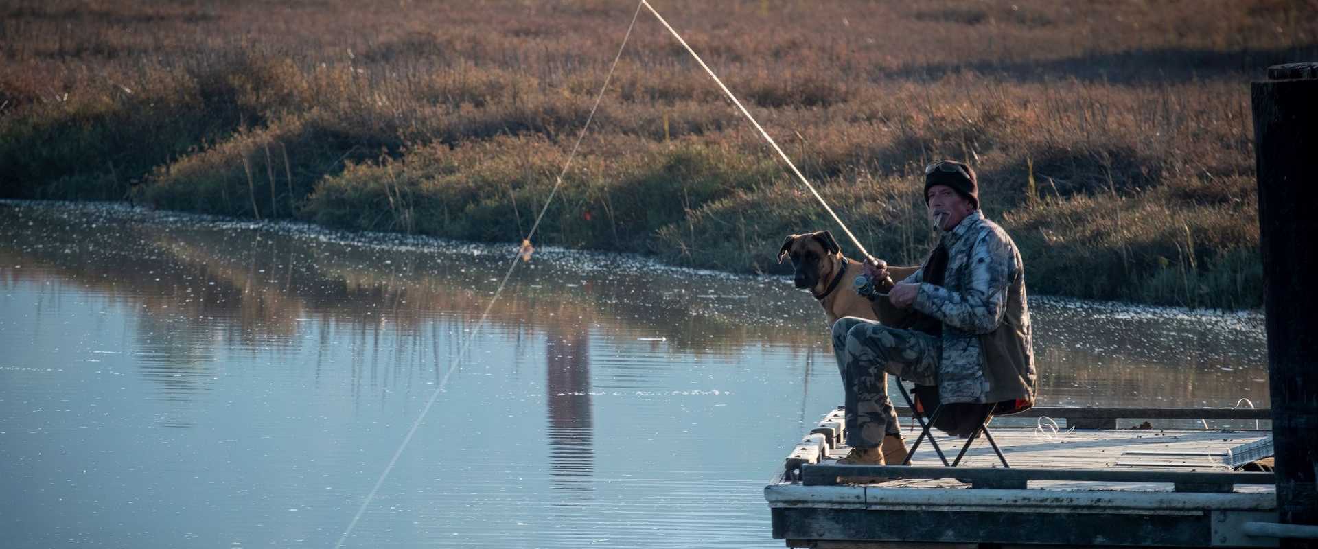 Ein Mann genießt das Freizeitangeln mit Hund an einem ruhigen Steg am See