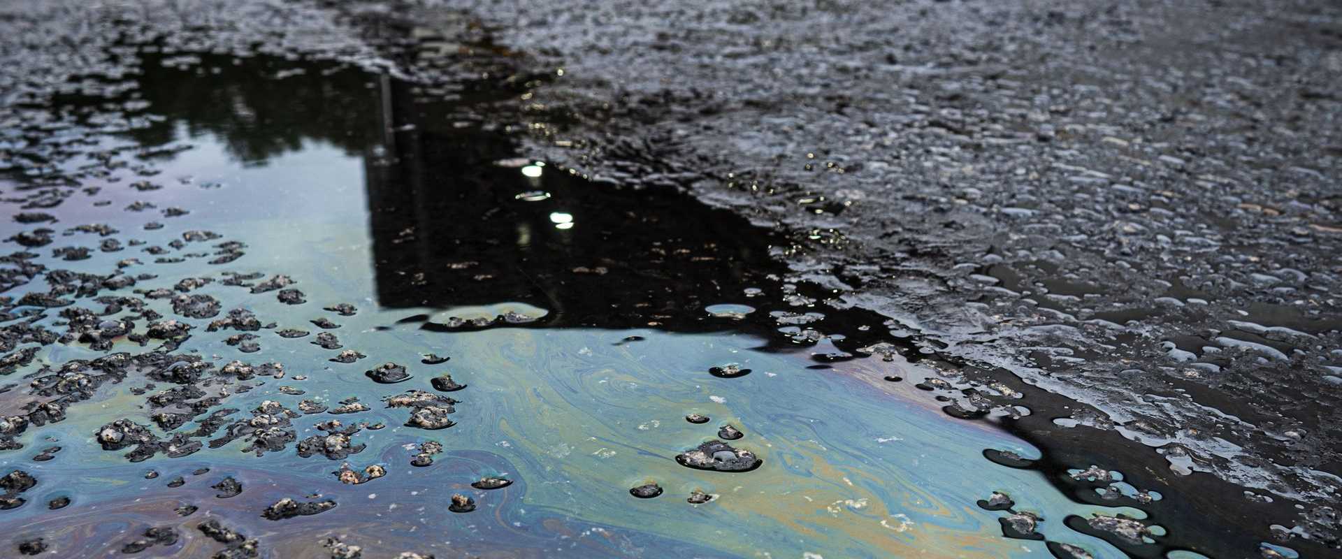 Ein leuchtend schimmernder Ölteppich auf rauer Asphaltfläche verdeutlicht die Umweltverschmutzung