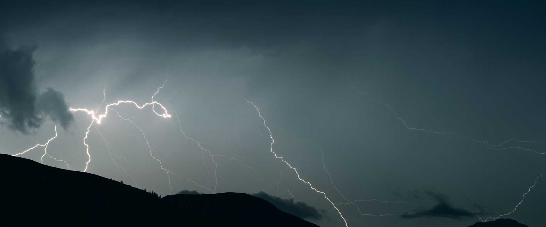 Faszinierender Schnappschuss von Blitzen, die einen dunklen Himmel über Bergsilhouetten während eines Gewitters erhellen.