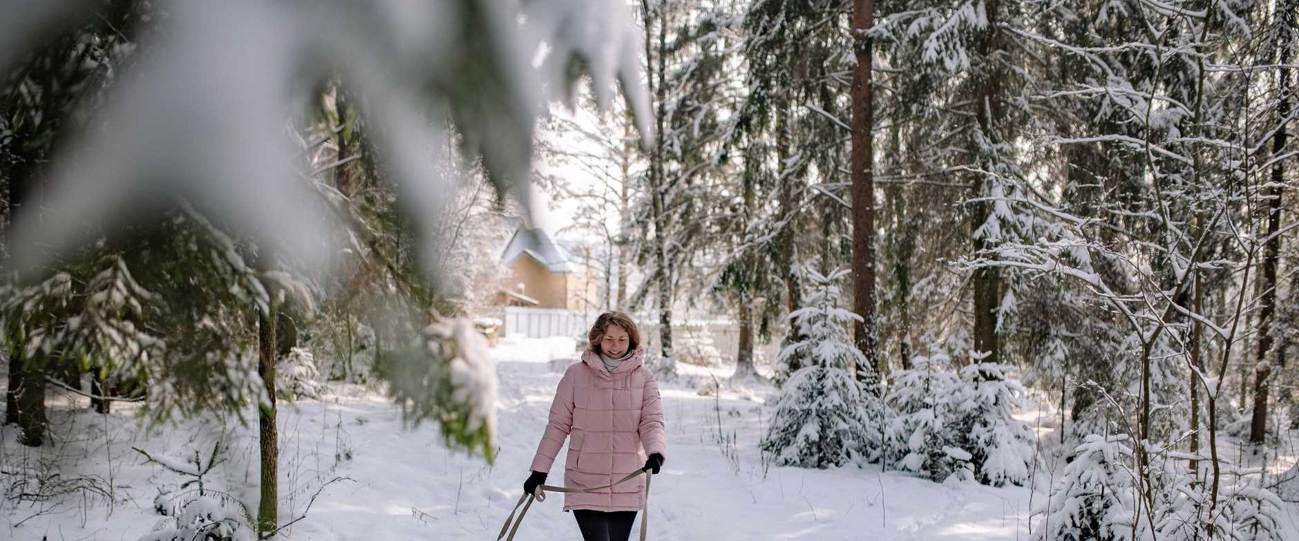 Frau, die einen Deutschen Schäferhund in einem verschneiten Wald spazieren führt und einen ruhigen Wintertag genießt.